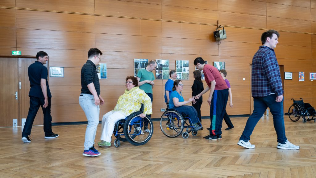 Rollstuhlfahrerinnen und Laufende finden sich zu Tanzpaaren zusammen