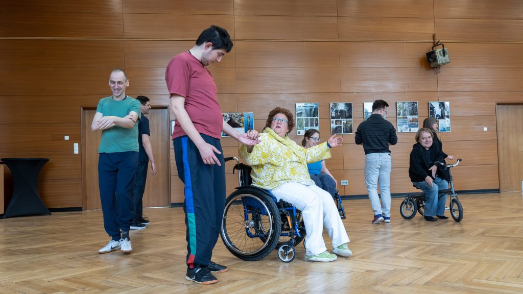 Eine Tänzerin im Rollstuhl und ein Tänzer geben einander die Hand