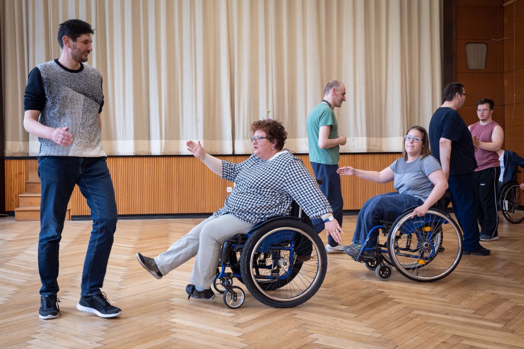 Zwei Tänzerinnen im Rollstuhl breiten ihre Arme seitlich aus